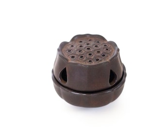 May include: A brown ceramic incense burner shaped like a lotus flower with a circular top and multiple holes. The burner has a textured surface and a dark brown glaze.