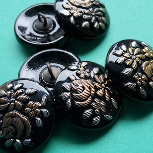 May include: Four black buttons with a gold and silver floral design. The buttons have a shiny finish and are ideal for sewing projects.