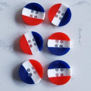 May include: Six circular buttons in red, white, and blue. Each button features a white central section with four holes, and a diagonal split of red and blue. The buttons are displayed on a light-coloured surface.