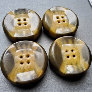 May include: Four brown and gold plastic buttons with four holes each. The buttons have a swirl pattern.