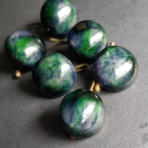 Peut inclure: Six boutons ronds, irisés vert et bleu, avec des tiges en métal doré.