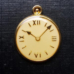 Könnte beinhalten: Goldfarbener Anhänger in Form einer Taschenuhr. Das cremefarbene Zifferblatt zeigt schwarze römische Ziffern und goldene Zeiger, die etwa 10:08 Uhr anzeigen. Der Anhänger hat eine Schlaufe für eine Kette und misst etwa 3 cm im Durchmesser.