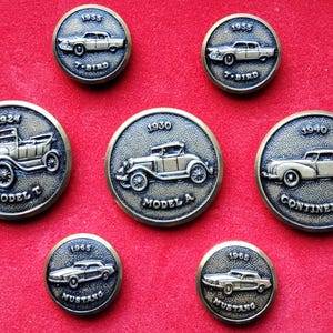 May include: Seven antique brass-effect car medallions. Each round medallion features a classic car design with the year and model name, including a 1924 Model T, 1930 Model A, and 1965 Mustang. The medallions are on a red background.
