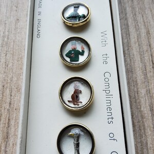 Peut inclure: Ensemble de quatre boutons fantaisie vintage avec des bordures dor&eacute;es. Chaque bouton pr&eacute;sente un design miniature diff&eacute;rent : une tortue, un homme en vert, un lapin et un canard. La bo&icirc;te indique "Made in England" et "With the Compliments of GU".