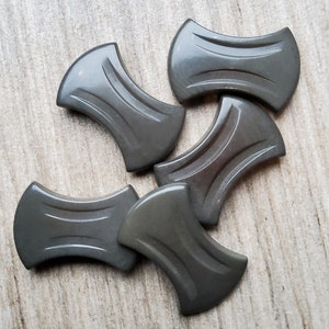 Peut inclure: Cinq boutons en plastique gris avec une forme unique, incurvée, en sablier. Les boutons ont une finition lisse et brillante.