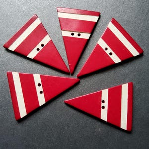 May include: Five red, triangular buttons with white stripes and two black buttonholes. The buttons are arranged in a circular pattern on a dark gray surface. The buttons have a Santa Claus theme.