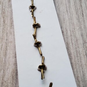 May include: A set of seven gold-colored metal hooks, arranged vertically on a white card. The hooks are designed to be used for hanging items.