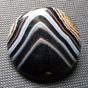 May include: A black, white, and brown agate stone with a chevron pattern. The stone is polished and has a smooth surface.