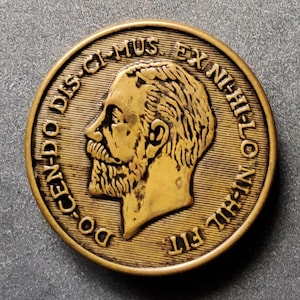 Puede incluir: Una moneda de color dorado con el perfil de un hombre con barba en un lado y el texto "CEN-DO DS-CI MUS XNI-HI-LONI-HIL FIT" en el otro.