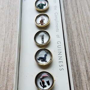Peut inclure: Un ensemble de six &eacute;pingles promotionnelles Guinness vintage avec des bords dor&eacute;s. Chaque &eacute;pingle pr&eacute;sente une image diff&eacute;rente sous un couvercle transparent en forme de d&ocirc;me. Les &eacute;pingles sont pr&eacute;sent&eacute;es dans une bo&icirc;te blanche avec le texte "With the Compliments of GUINNESS".