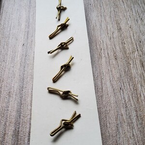 May include: Six vintage gold-toned tie clips arranged on a white card. The tie clips have a simple, elegant design with a knot detail. The background is a light-colored wooden surface, providing a neutral backdrop for the accessories.