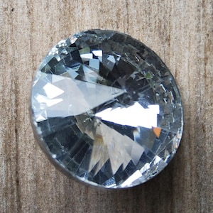 Könnte beinhalten: Ein runder Knopf aus klarem Glas mit facettiertem Design. Der Knopf hat eine glänzende, reflektierende Oberfläche.