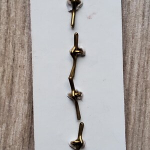 May include: A set of six gold-toned metal clasps, each with a unique knot design, displayed on a white card.