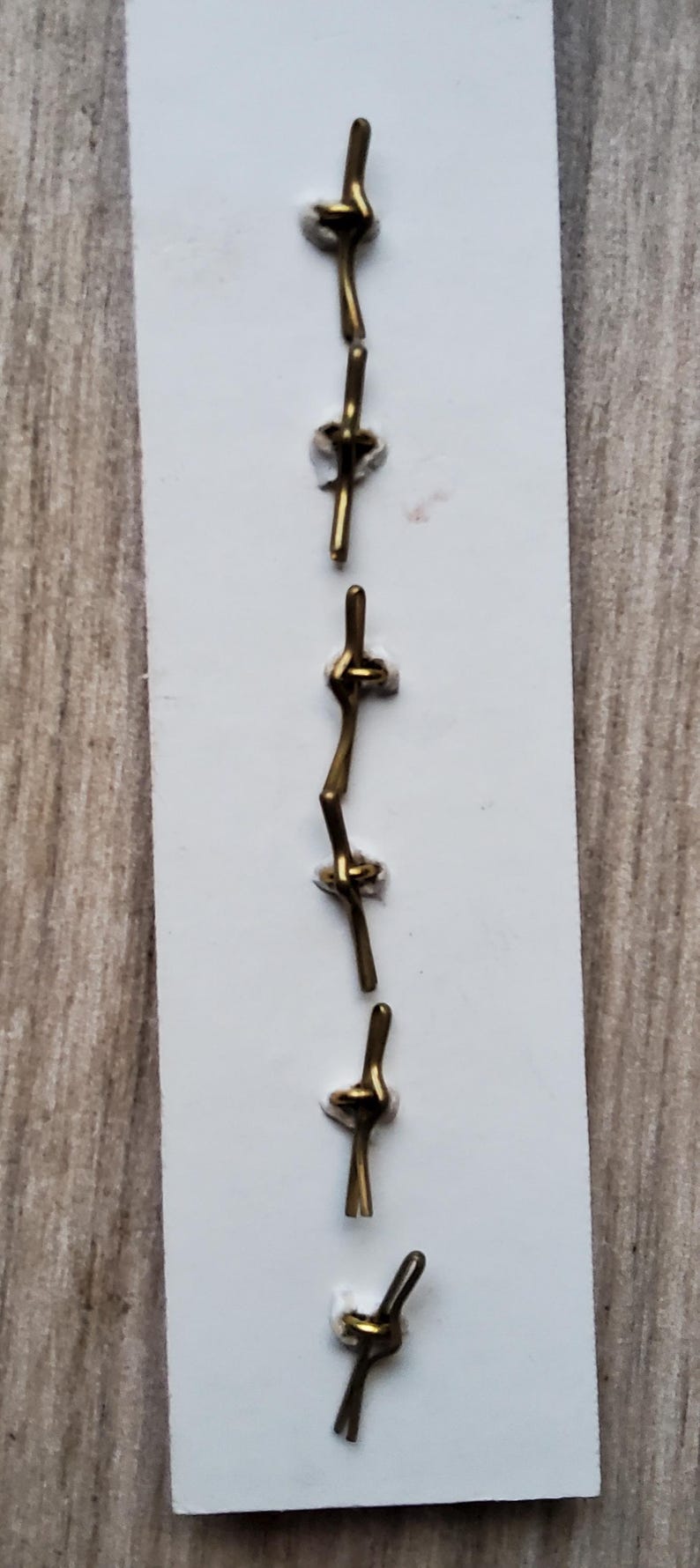 May include: A set of six gold-toned metal clasps, each with a unique knot design, displayed on a white card.