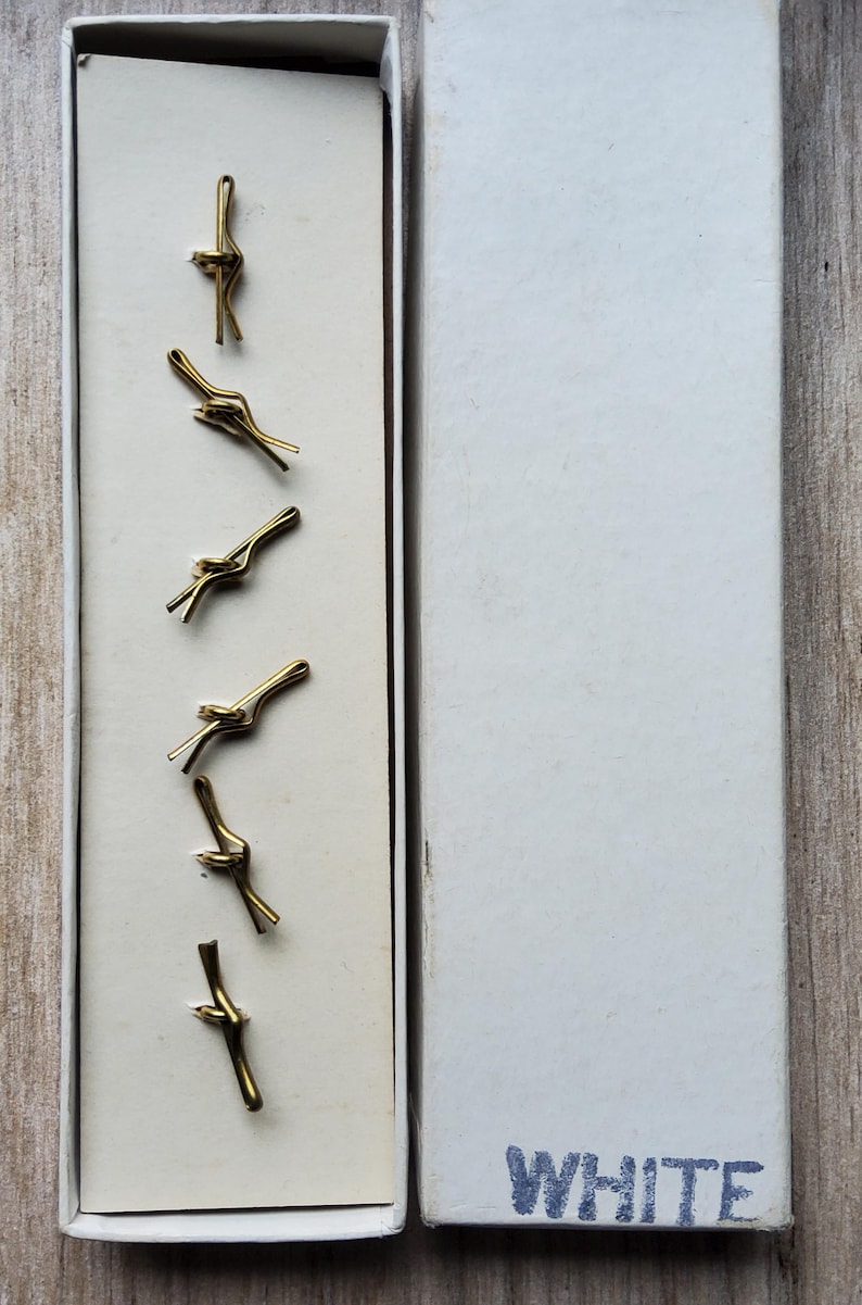 Peut inclure: Bo&icirc;te ouverte contenant six pinces &agrave; cravate dor&eacute;es en forme de n&oelig;ud. Les pinces sont dispos&eacute;es verticalement sur un fond cr&egrave;me. La bo&icirc;te blanche porte le mot "WHITE" imprim&eacute; sur le couvercle.