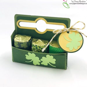 May include: A green and gold paper gift box with a handle, decorated with shamrocks. The box is filled with small wrapped chocolates and has a tag with a shamrock design.  Paper Closet Designs by Tracy Rushton www.paperclosetdesigns.com