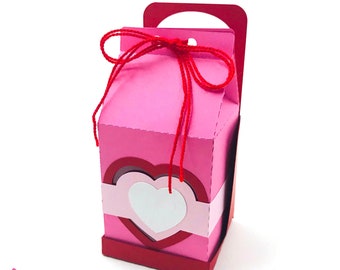 May include: A pink and red cardboard gift box with a heart-shaped cutout and a red ribbon. The box has a handle and is decorated with a red ribbon.