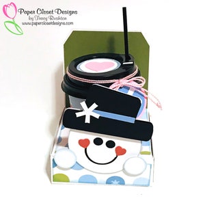 May include: A snowman-themed paper craft with a coffee cup, a black hat, and a pink heart on the lid. The coffee cup is sitting on a blue and white polka dot background.