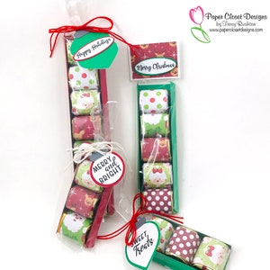 May include: Christmas-themed gift boxes filled with wrapped treats. Each box contains five candies with festive designs, including Santa Claus, reindeer, and polka dots. The boxes are adorned with tags that read "Happy Holidays," "Merry Christmas," "Merry and Bright," and "Sweet Treats."