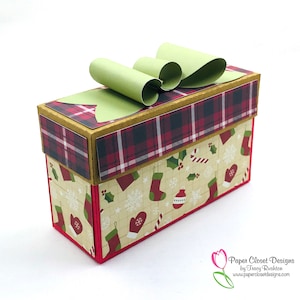 May include: A red and green plaid gift box with a green bow on top. The box is decorated with a Christmas pattern of stockings, holly, candy canes, and snowflakes. The box is labelled "Paper Closet Designs by Tracy Rushton".