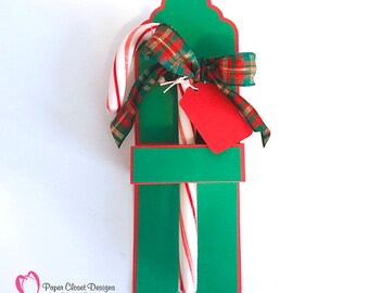 May include: A green and red candy cane holder with a red bow and a red tag. The holder is decorated with a scalloped edge and a white border. The text "Paper Closet Designs by Tracy Rushton www.ideacloset.blogspot.com" is printed on the bottom of the holder.