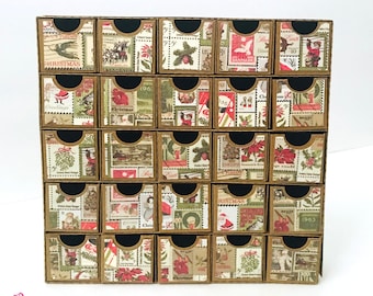 May include: A vintage-style Christmas advent calendar with 24 drawers, each decorated with a different patterned paper featuring images of stamps, wreaths, and holiday greetings. The drawers are arranged in a 4x6 grid and are made of brown cardboard.