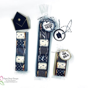 May include: Three graduation gift sets. One has a black mortarboard box. The other two contain wrapped sweets with star and graduation cap patterns. Tags read "Congrats Grad" and "You Did It."