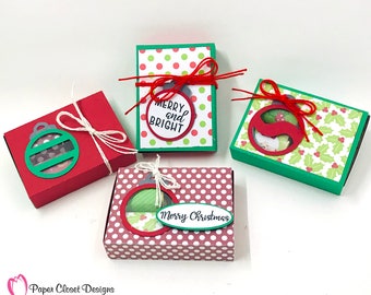 May include: Four small red and green gift boxes with a Christmas ornament design. The boxes are decorated with red and white polka dots, green holly leaves, and the text "Merry and Bright" and "Merry Christmas".