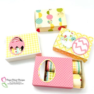 May include: Four Easter-themed gift boxes with different designs. The boxes are decorated with polka dots, gingham, and floral patterns. The boxes have a window cut out in the shape of an egg. The boxes are open to reveal small gifts inside.