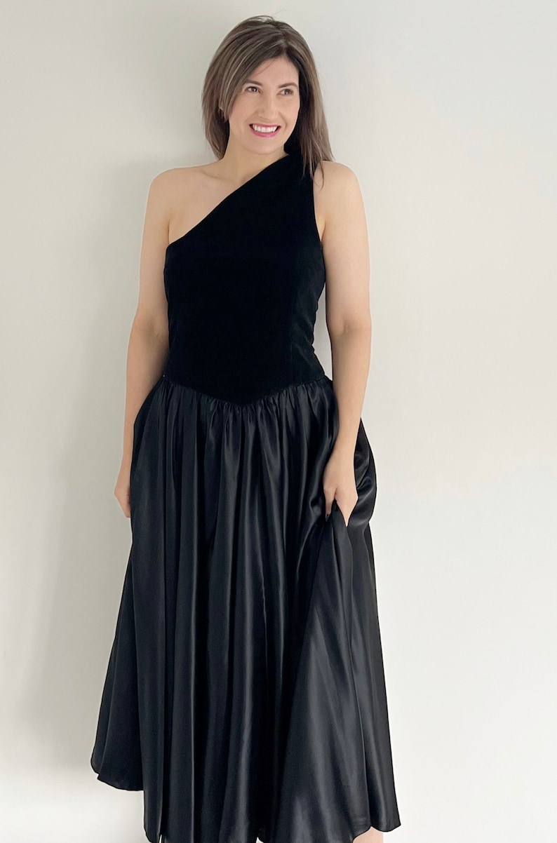 A black velvet occasion dress.  The dress dates from the 80s and has a velvet bodice with a full circle skirt section.  The dress has one shoulder and ideal for a UK 12 14