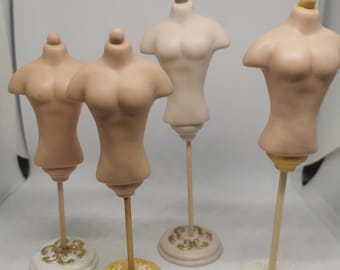 以下が含まれることがあります： ベージュとクリーム色の4つのミニチュアトルソー。各フォームは木のダボと装飾的なベースに取り付けられています。ベースは白、金、クリーム色で、装飾的なデザインが施されています。フォームにはA、B、C、Dのラベルが付いています。