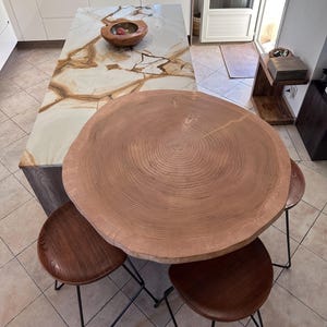 Peut inclure: Une table ronde en bois avec un motif de grain de bois naturel et un design en forme d'anneaux d'arbre. La table est entourée de trois chaises en bois brun avec des pieds en métal noir.