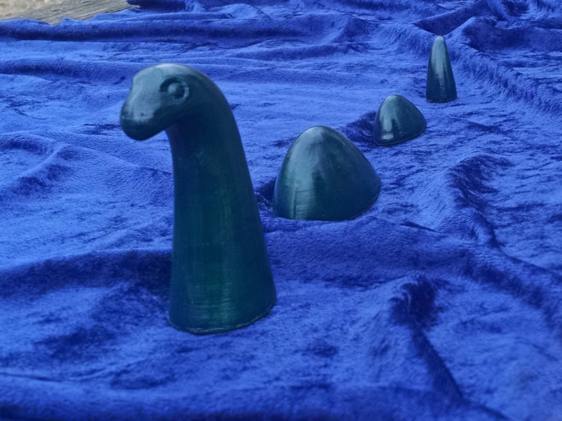 May include: A set of four teal blue ceramic sculptures of a mythical sea creature, resembling a long-necked dinosaur, on a blue velvet background.