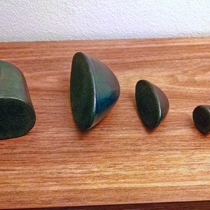 May include: Four green ceramic sculptures of varying sizes and shapes. The sculptures are arranged in a row on a wooden surface.