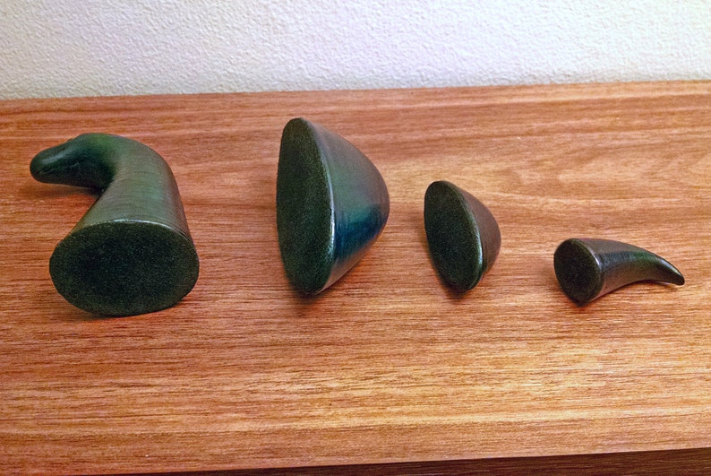May include: Four green ceramic sculptures of varying sizes and shapes. The sculptures are arranged in a row on a wooden surface.
