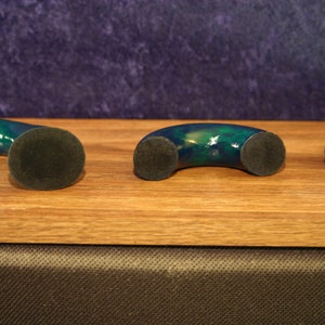 May include: Three decorative, curved objects with a dark green and blue marbled finish. Each object has a circular, dark gray base. The objects are arranged on a light brown wooden surface.