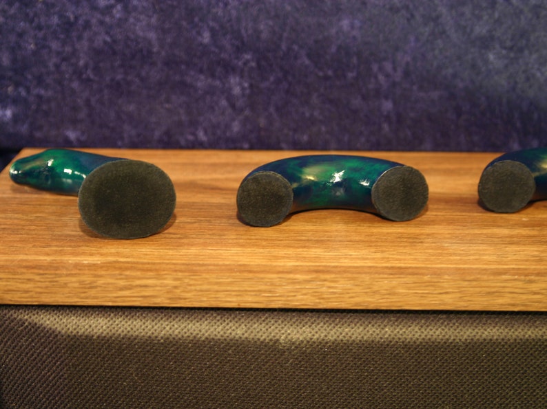 May include: Three decorative, curved objects with a dark green and blue marbled finish. Each object has a circular, dark gray base. The objects are arranged on a light brown wooden surface.