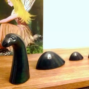 May include: A dark green ceramic figurine of a mythical sea monster, the Loch Ness Monster, with a long neck and a small head. The figurine is made up of five pieces, including the head, neck, and three body segments.