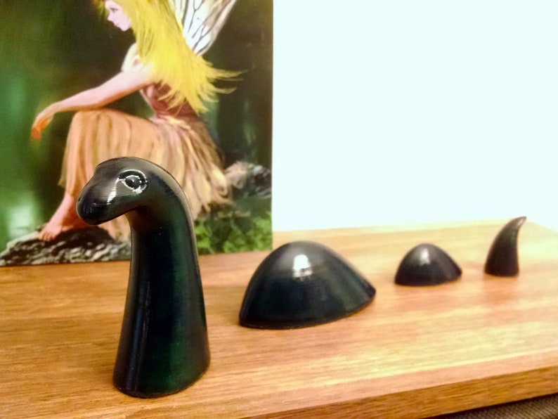 May include: A dark green ceramic figurine of a mythical sea monster, the Loch Ness Monster, with a long neck and a small head. The figurine is made up of five pieces, including the head, neck, and three body segments.