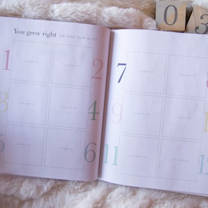 May include: A white baby memory book with a grid of 12 squares, each with a number from 1 to 12. The text "You grew right before our eyes" is printed at the top of the page.