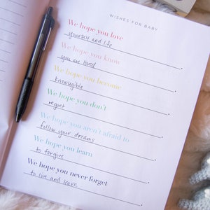 May include: A white journal with black lines and the text "Wishes for Baby" at the top. The journal has handwritten messages in different colors, including "We hope you love yourself and life", "We hope you know you are loved", "We hope you become knowledgeable", "We hope you don't regret", "We hope you aren't afraid to follow your dreams", "We hope you learn to forgive", and "We hope you never forget to live and learn".