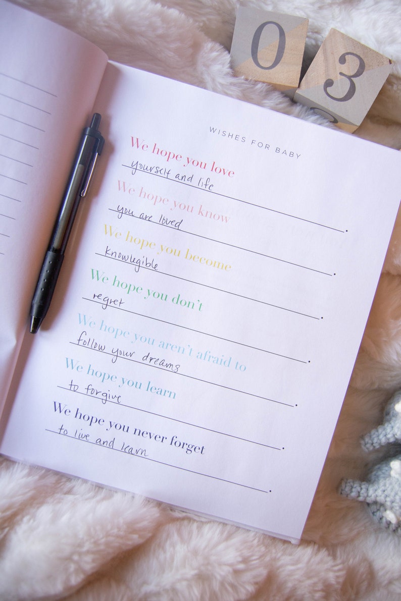 May include: A white journal with black lines and the text "Wishes for Baby" at the top. The journal has handwritten messages in different colors, including "We hope you love yourself and life", "We hope you know you are loved", "We hope you become knowledgeable", "We hope you don't regret", "We hope you aren't afraid to follow your dreams", "We hope you learn to forgive", and "We hope you never forget to live and learn".