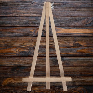 May include: A wooden easel with a simple design, ideal for displaying small artwork or photographs. The easel is made of light brown wood and has a natural finish.