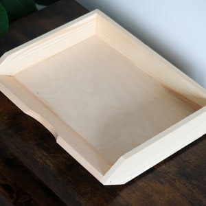 Könnte beinhalten: Ein Tablett aus Naturholz mit leicht abgeschrägter Kante. Das Tablett ist aus unbehandeltem Holz und hat eine glatte Oberfläche.