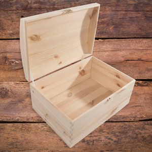 Könnte beinhalten: Eine leere Holzkiste mit einem Scharnierdeckel. Die Kiste ist aus hellem Holz gefertigt und hat ein schlichtes Design. Der Deckel ist geöffnet und das Innere der Kiste ist sichtbar.