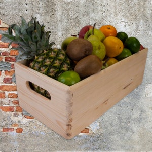 Pode incluir: Uma caixa de madeira cheia de fruta fresca, incluindo abacaxi, kiwi, peras, limas e laranjas. A caixa é feita de madeira natural e tem uma alça lateral.