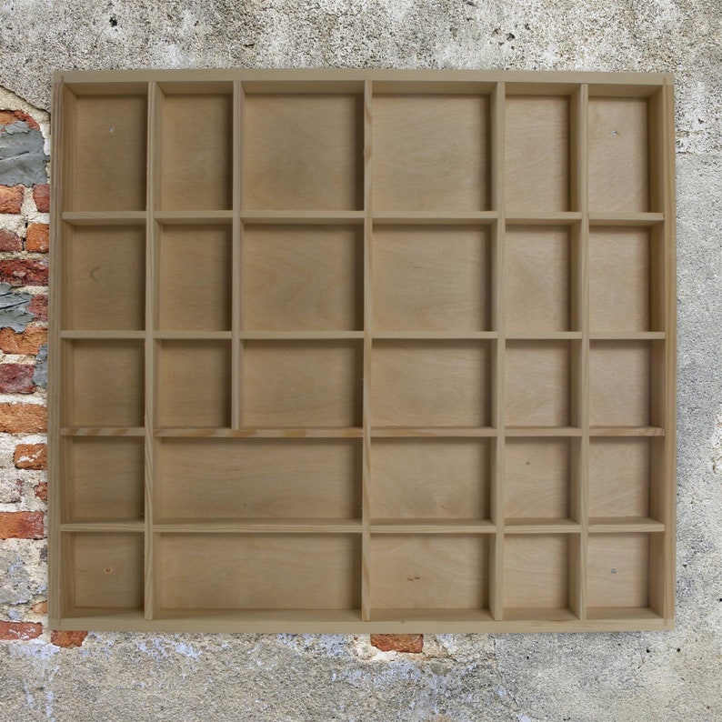 May include: A wooden display shelf with 18 square compartments. The shelf is made of light brown wood and has a simple, rustic design.
