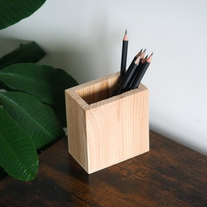 Puede incluir: Un porta lápices de madera con un acabado natural. El porta lápices está lleno de lápices negros.