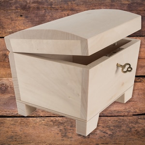 Könnte beinhalten: Eine Holzkiste mit einem Scharnierdeckel und einem Schlüsselloch. Die Kiste ist aus hellem Holz gefertigt und hat ein schlichtes Design. Der Deckel ist geöffnet und zeigt das Innere der Kiste.