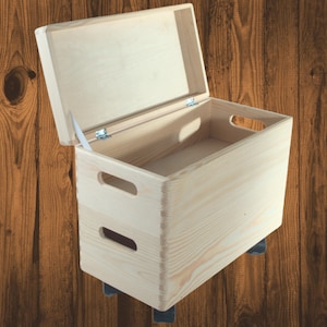 May include: A light-colored wooden storage box with a hinged lid, open to reveal the interior. The box has two handles on the sides and is mounted on small wheels. The wood grain is visible, and the box appears to be new.